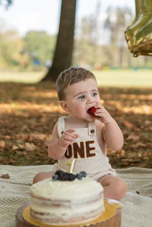 A baby reaches for a white cake during a first birthday smash cake session outdoors.