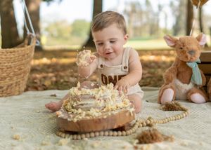 A baby enjoys a messy cake smash photoshoot in an outdoor autumn setting.