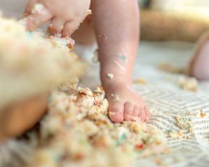 Close-up of small hands playing with cake crumbs and frosting on a light surface.