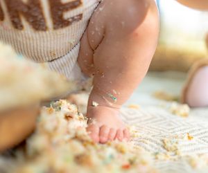 Hands touching and exploring cake crumbs on a white surface.