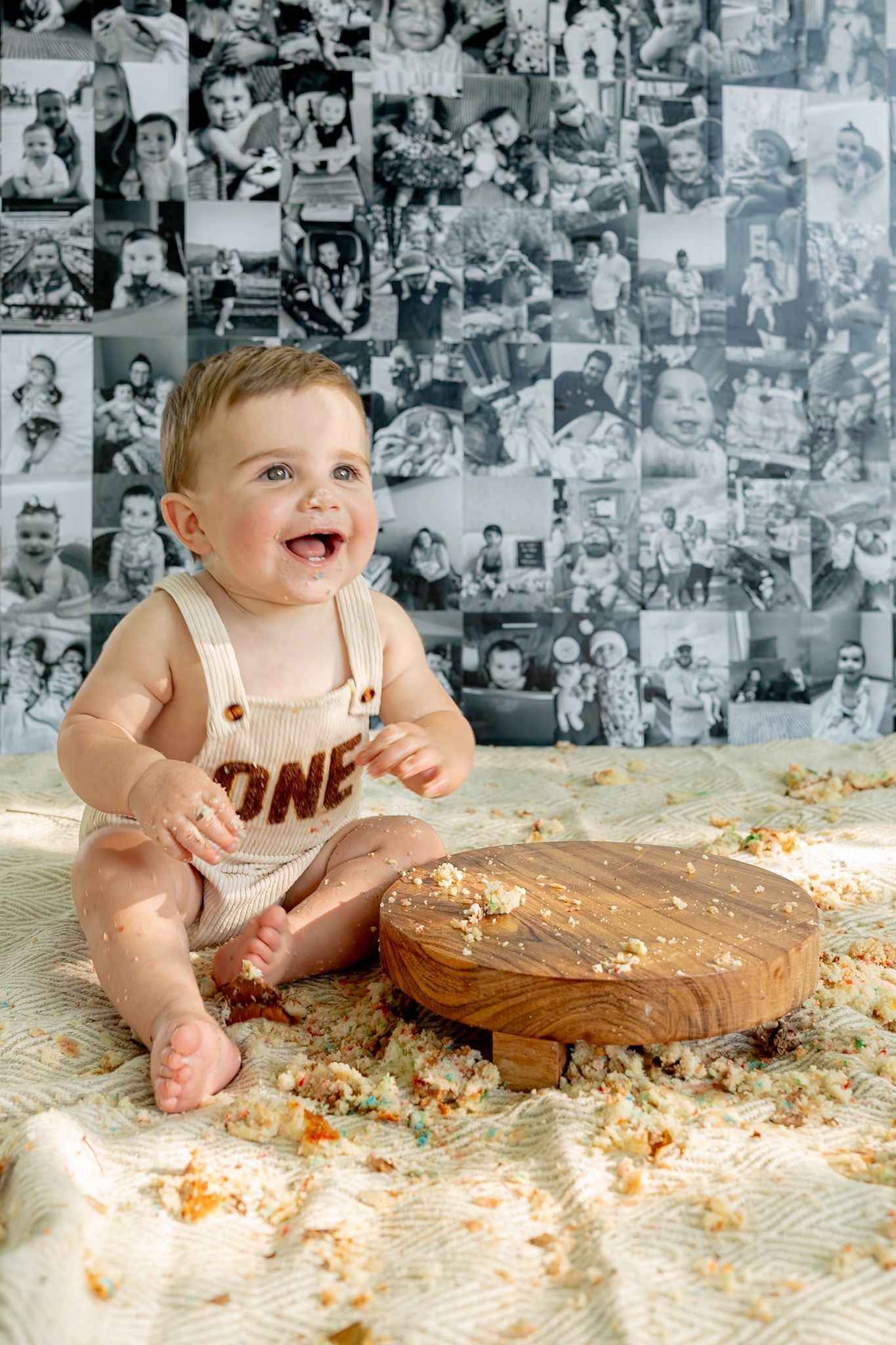 Baby in white outfit sitting with cake smash setup against black and white photo wall backdrop.