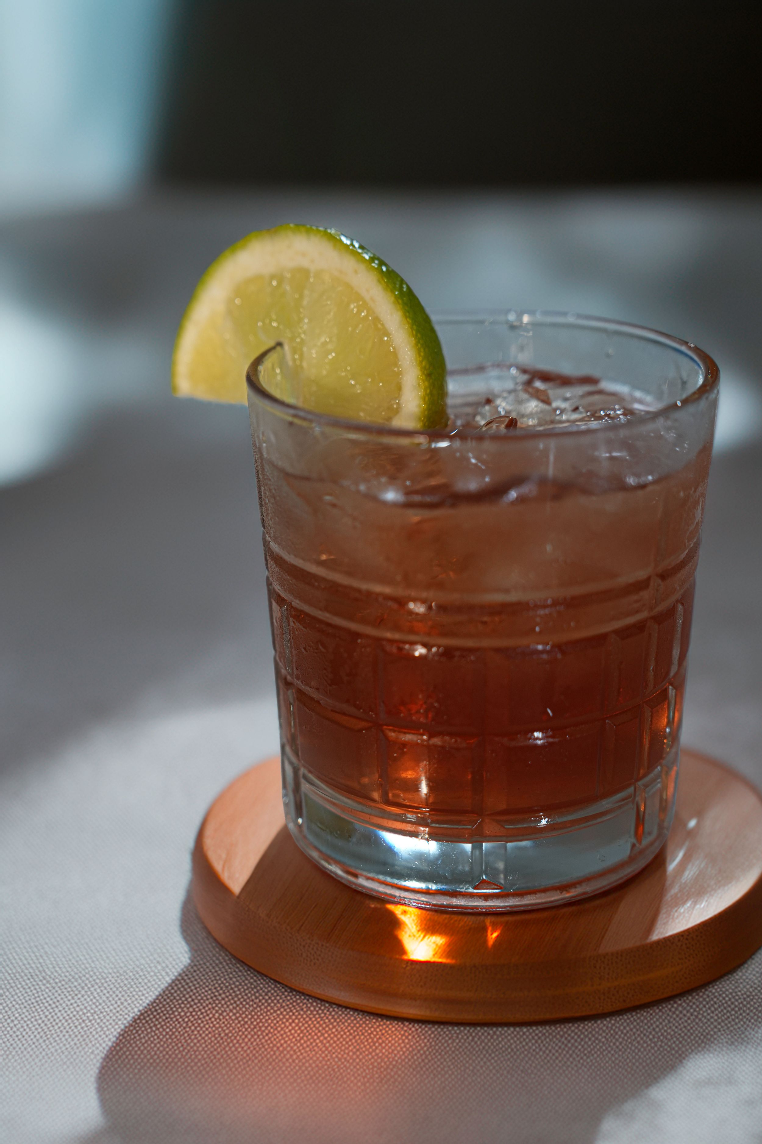 Close-up of amber-colored cocktails with lemon garnish in glass tumblers on white surface.