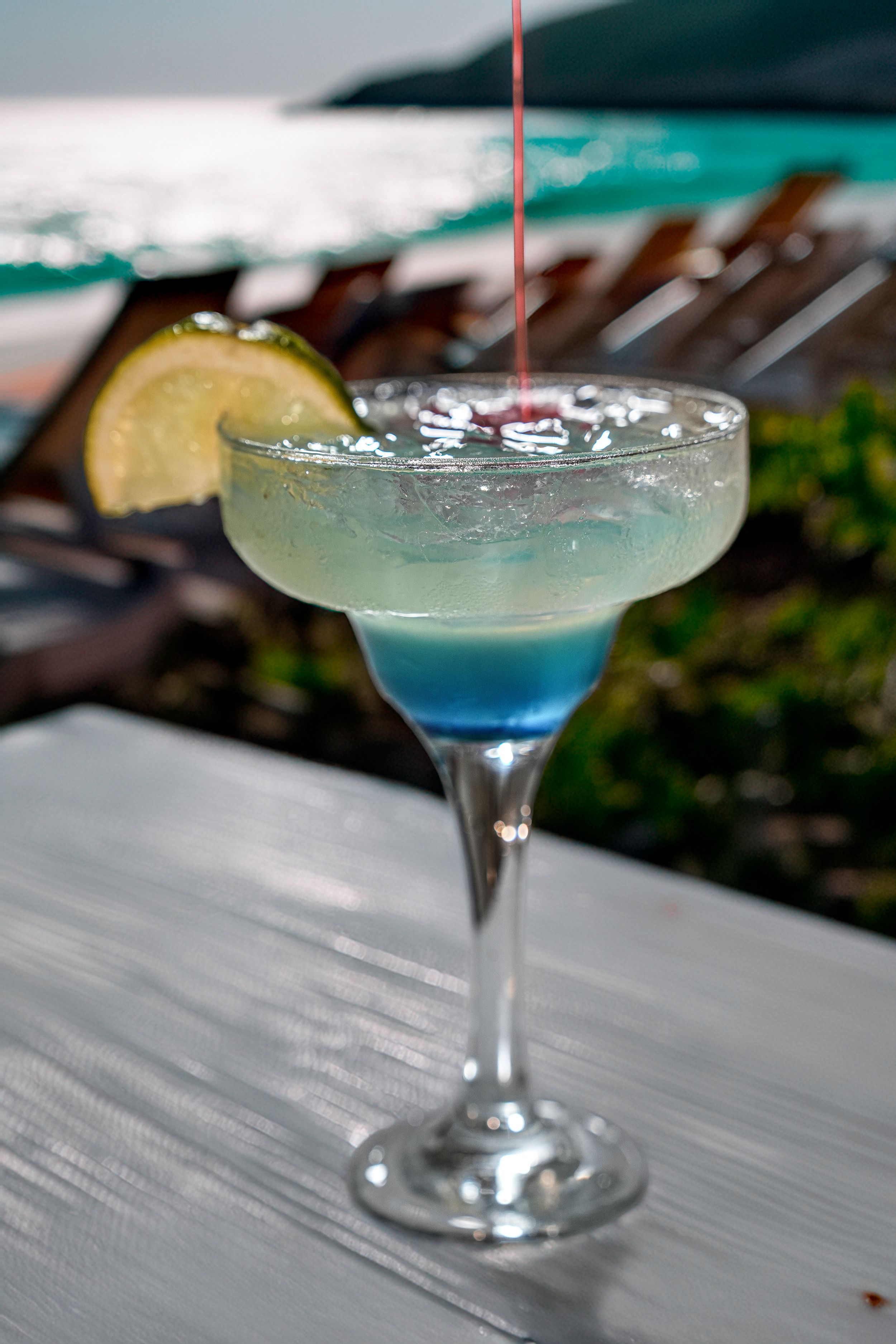 Clear martini glass with blue-tinted cocktail and lime garnish.