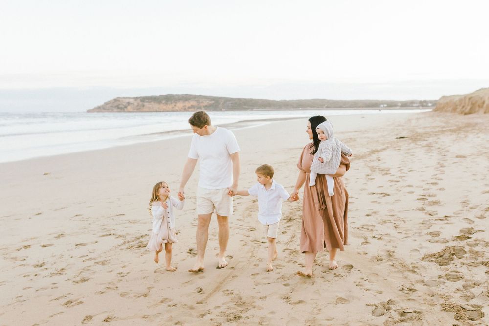Family walking together along a scenic beach shoreline during golden hour at sunset.