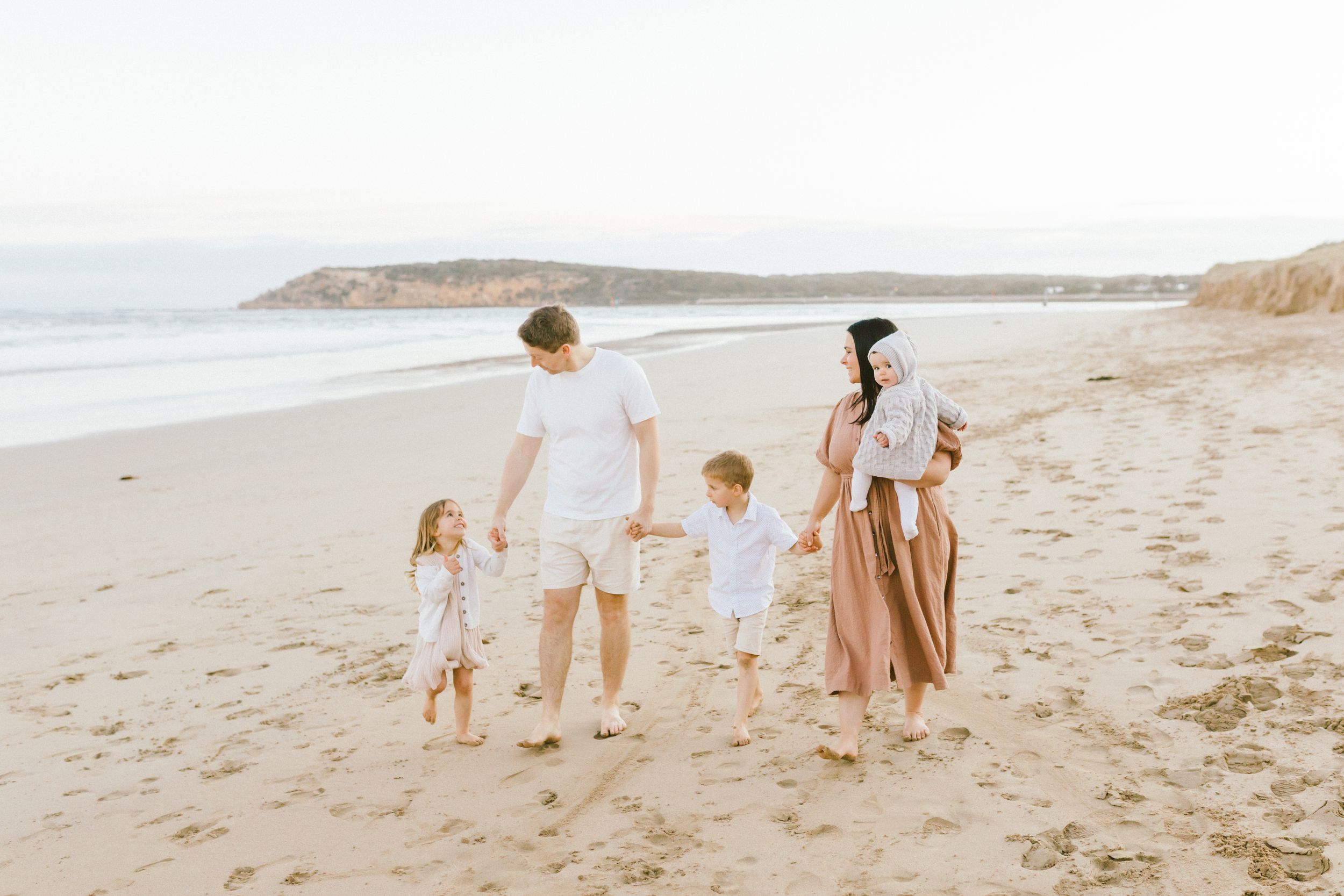 Family walking together along a scenic beach shoreline during golden hour at sunset.