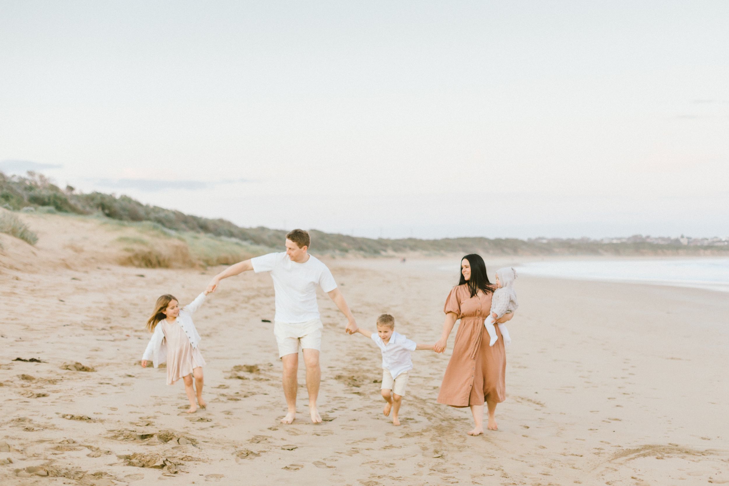 A group walks along a serene beach at sunset with warm golden light illuminating their path.