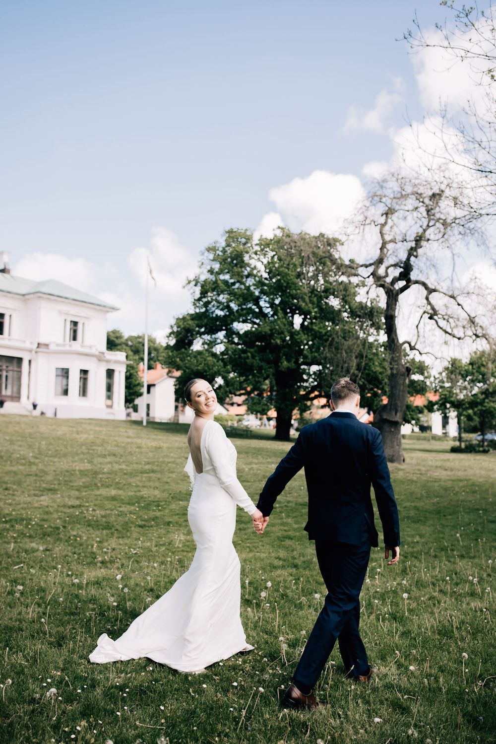 Couple walking and dancing together on grassy hill with white church building in background.