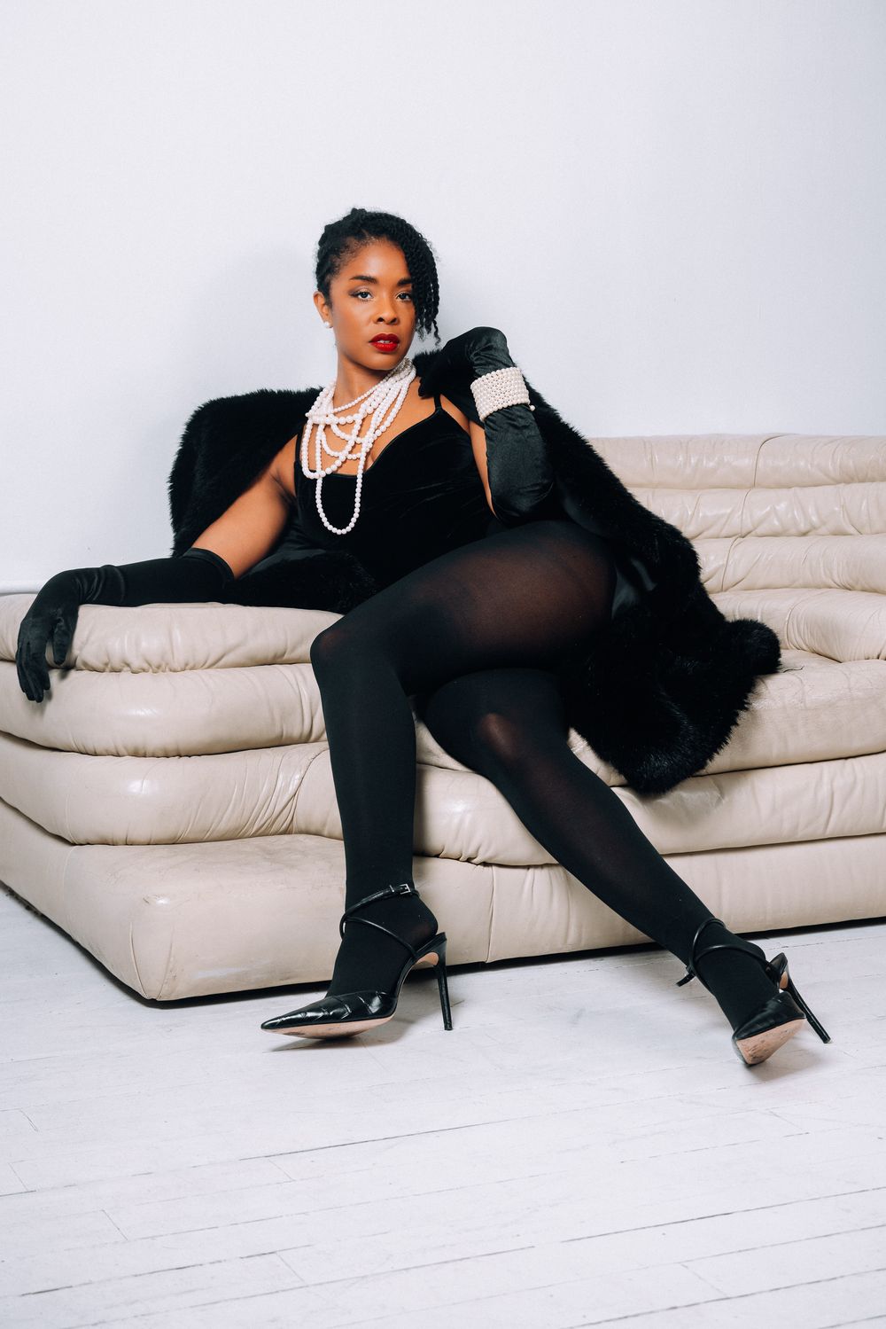 A model in a black outfit poses elegantly on a cream-colored couch in a fashion photography series.