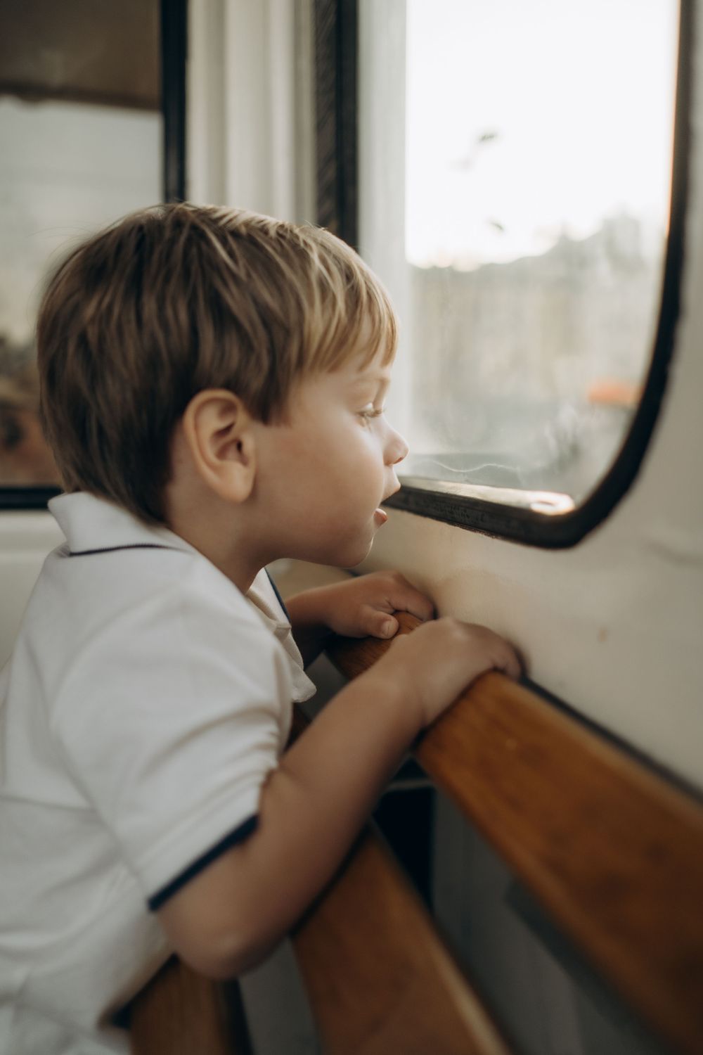 little boy looking outside a window on a boat in central Stockholm during family vacation photoshoot in Stockholm