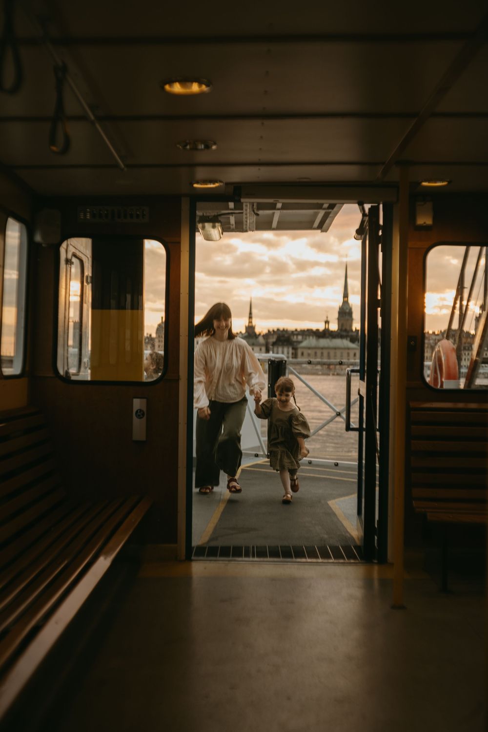 mom and daughter running through a door on a boat with Stockholm view in background during vacation photoshoot in Stockholm