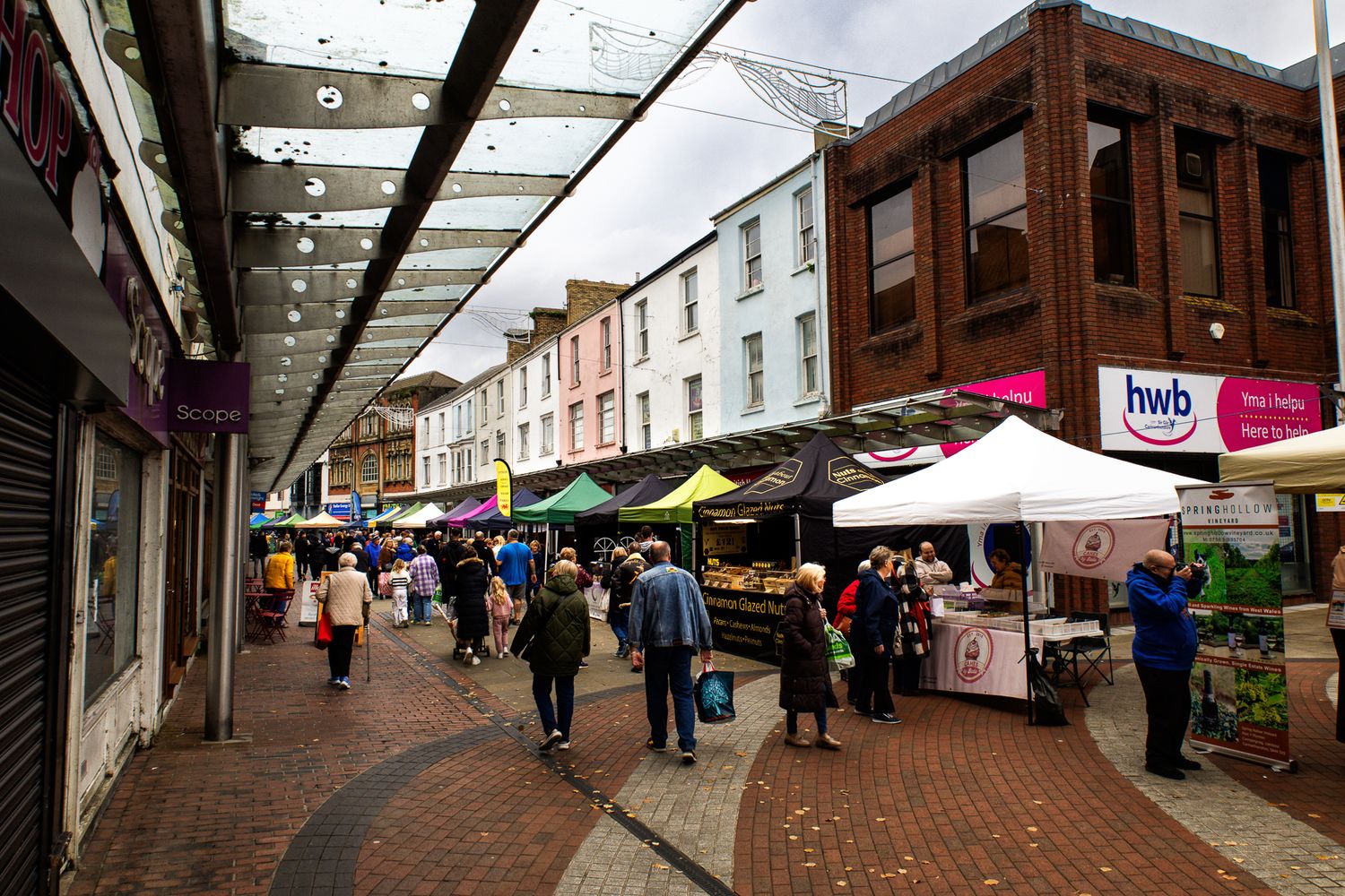 Outdoor street market with colorful stalls along a pedestrian street full of shoppers in Autumn, showing community life.