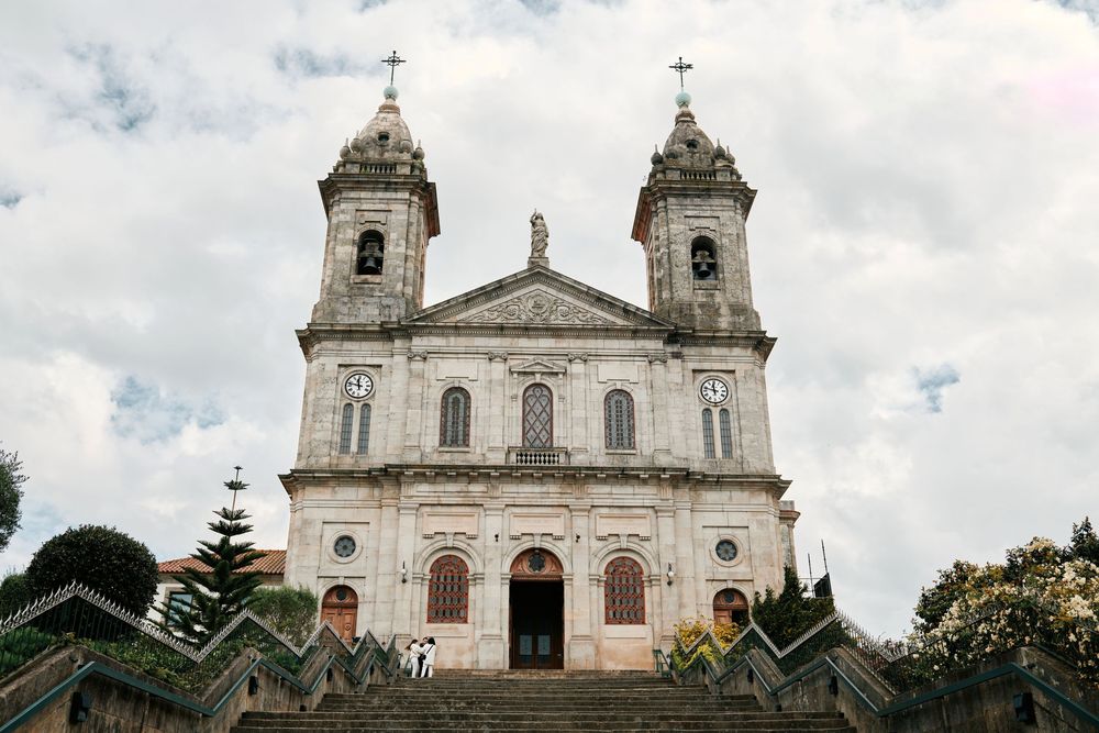 Grand white baroque Catholic church with twin bell towers and stone steps under a cloudy sky.