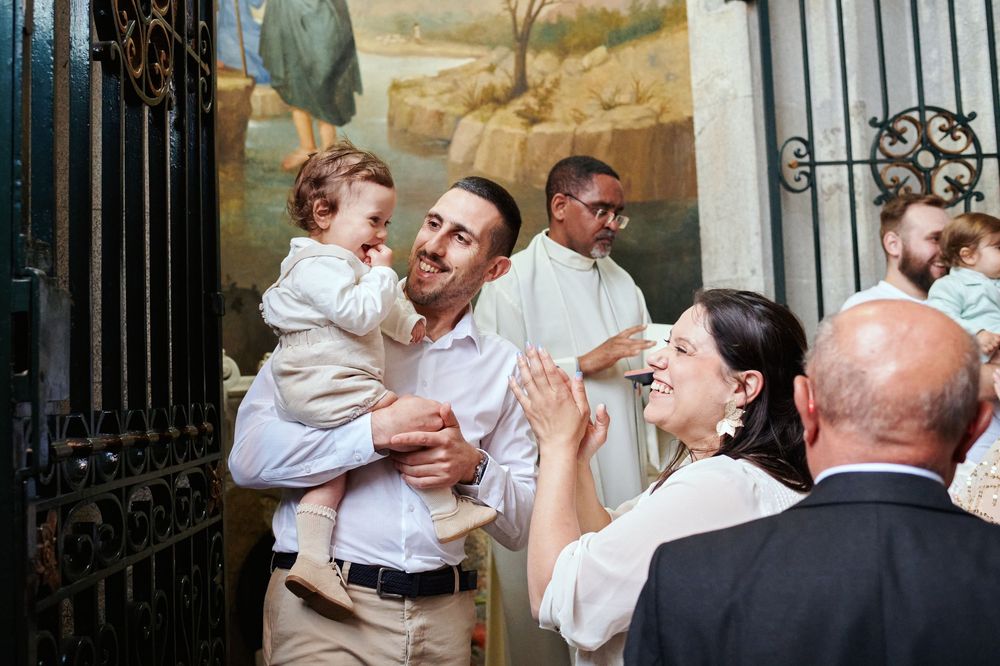 A joyful father holds his baptized baby while greeting smiling guests outside a church.