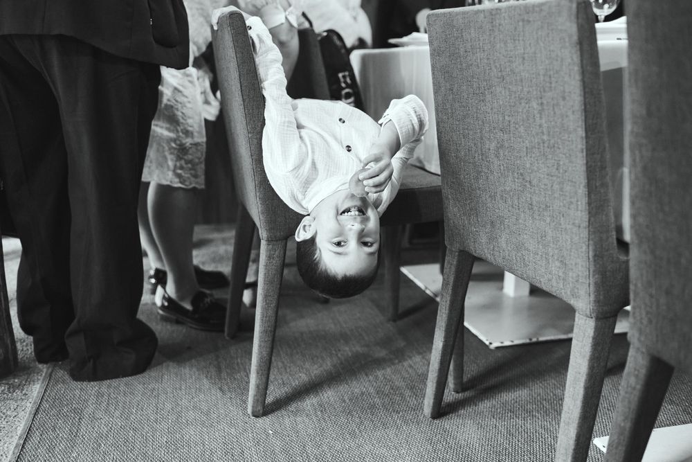 A playful child hangs upside down between chairs in a black and white photo.