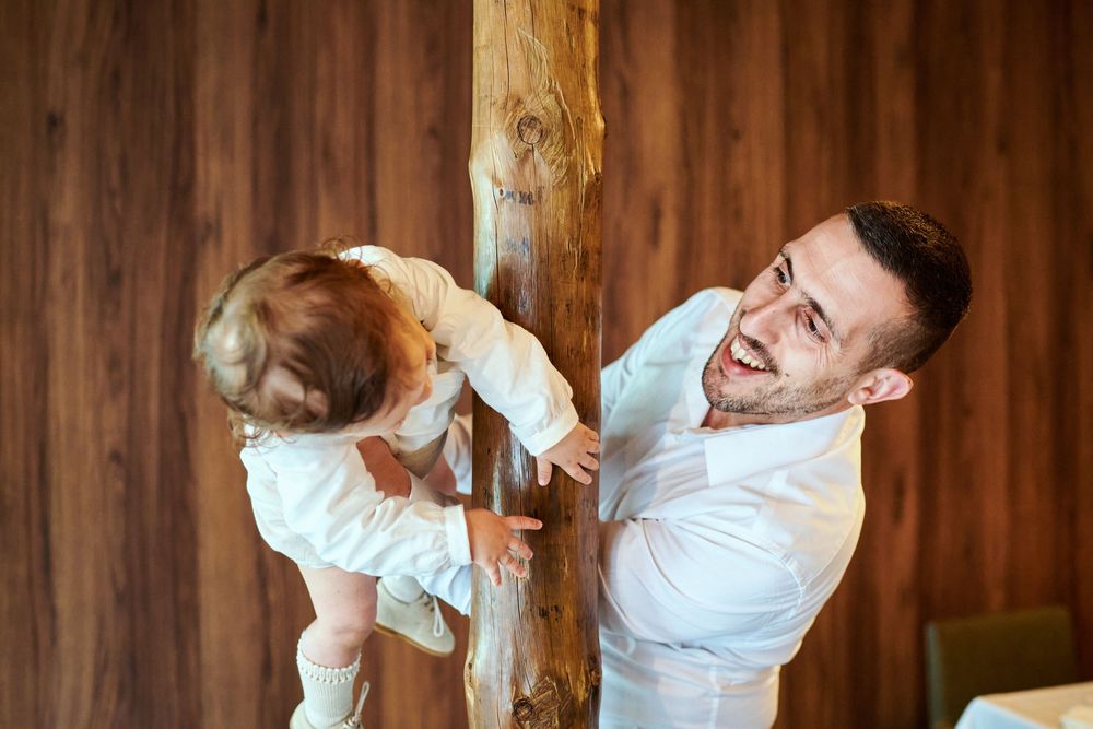 A laughing father lifts his baby near a wooden post, viewed from above.