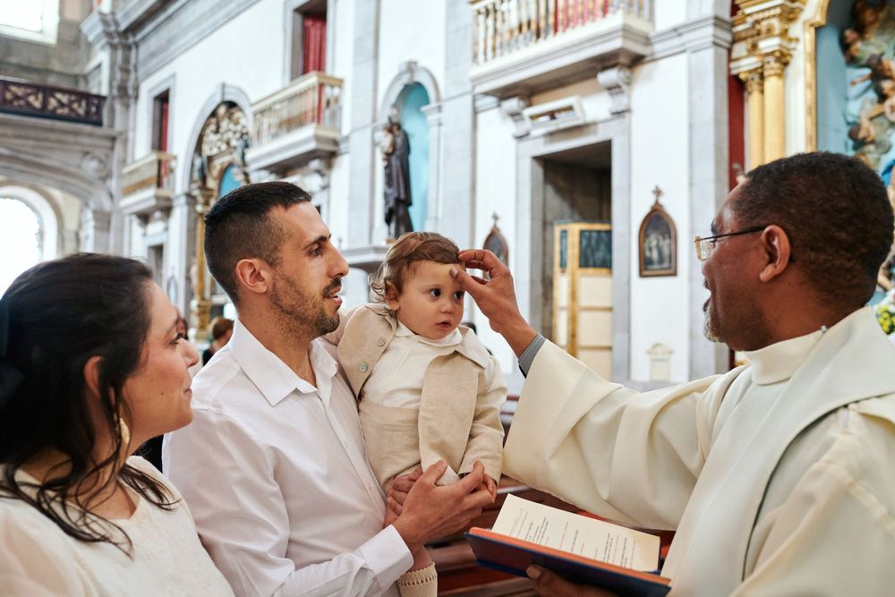 Catholic priest anointing a toddler's forehead during a baptism ceremony with parents present in church.