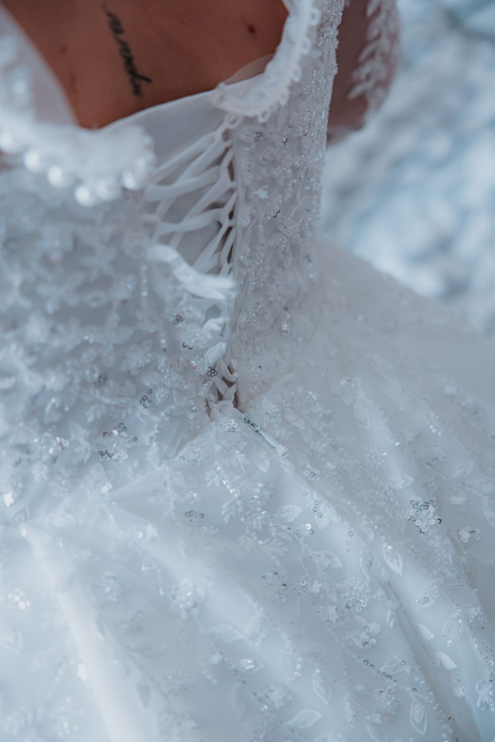 Intricate white lace and beadwork details of a wedding gown in soft natural light.