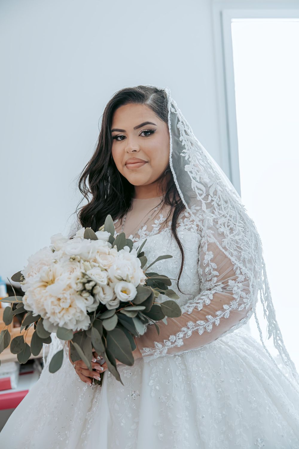 Bride in an elegant white lace wedding dress holding a cream and green floral bouquet.