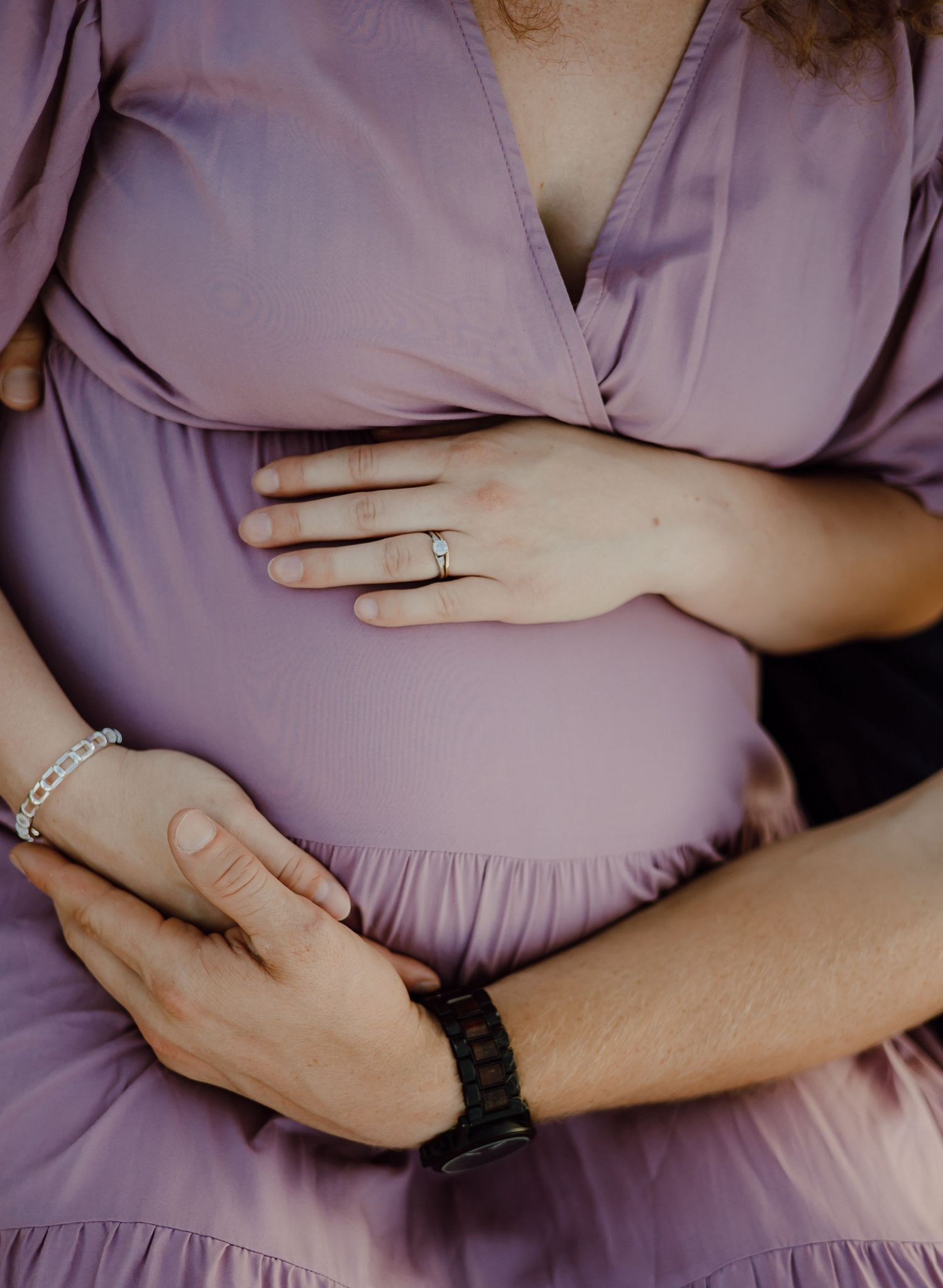 Close-up of hands with engagement ring resting on a purple dress.