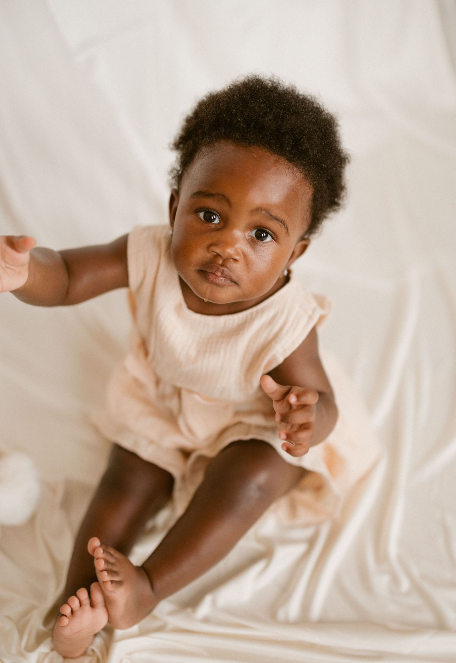 A series of sweet expressions from a baby in white clothing laying on white bedding.