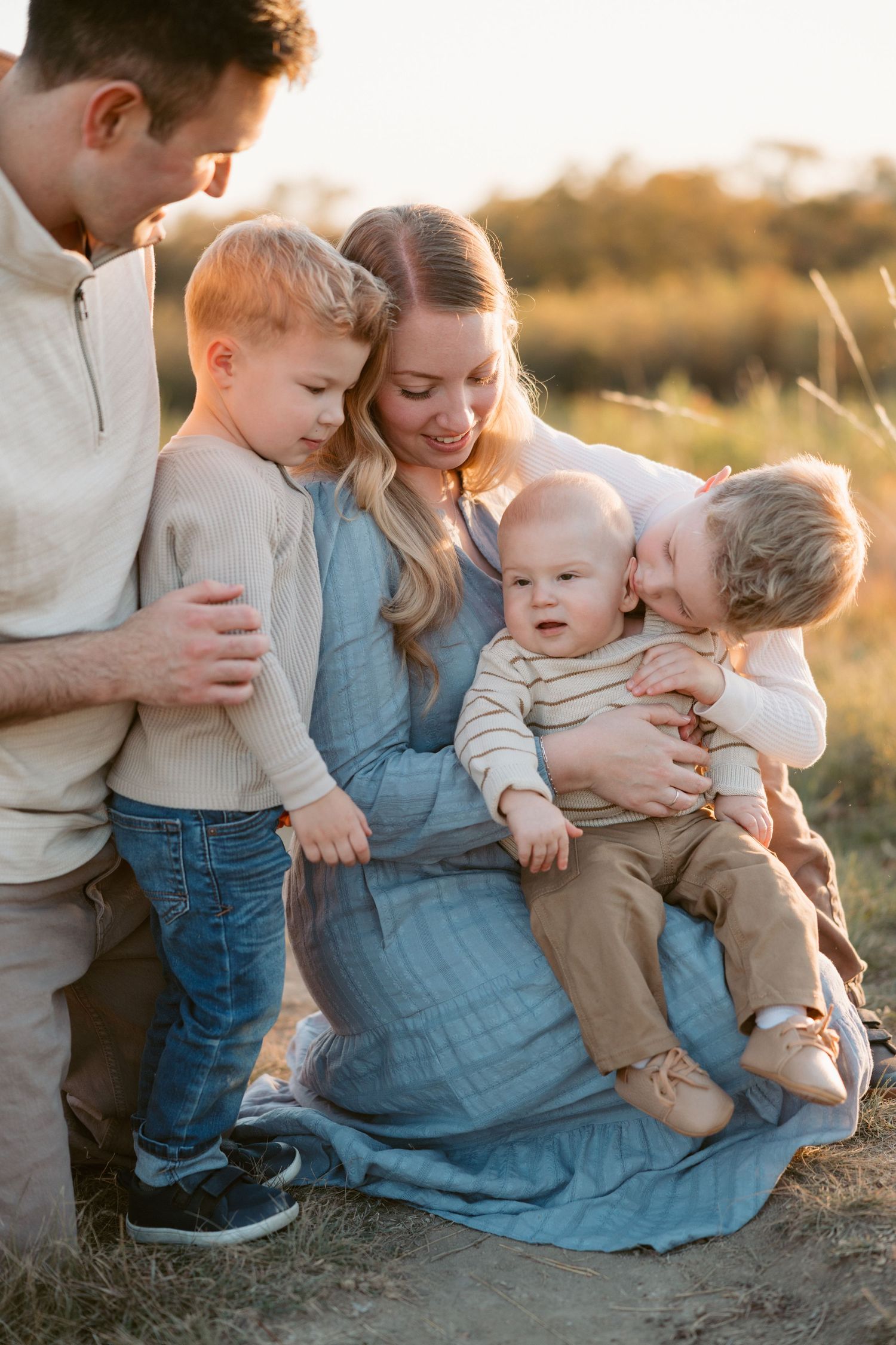 A family shares a tender moment together outdoors during golden hour in a natural setting.