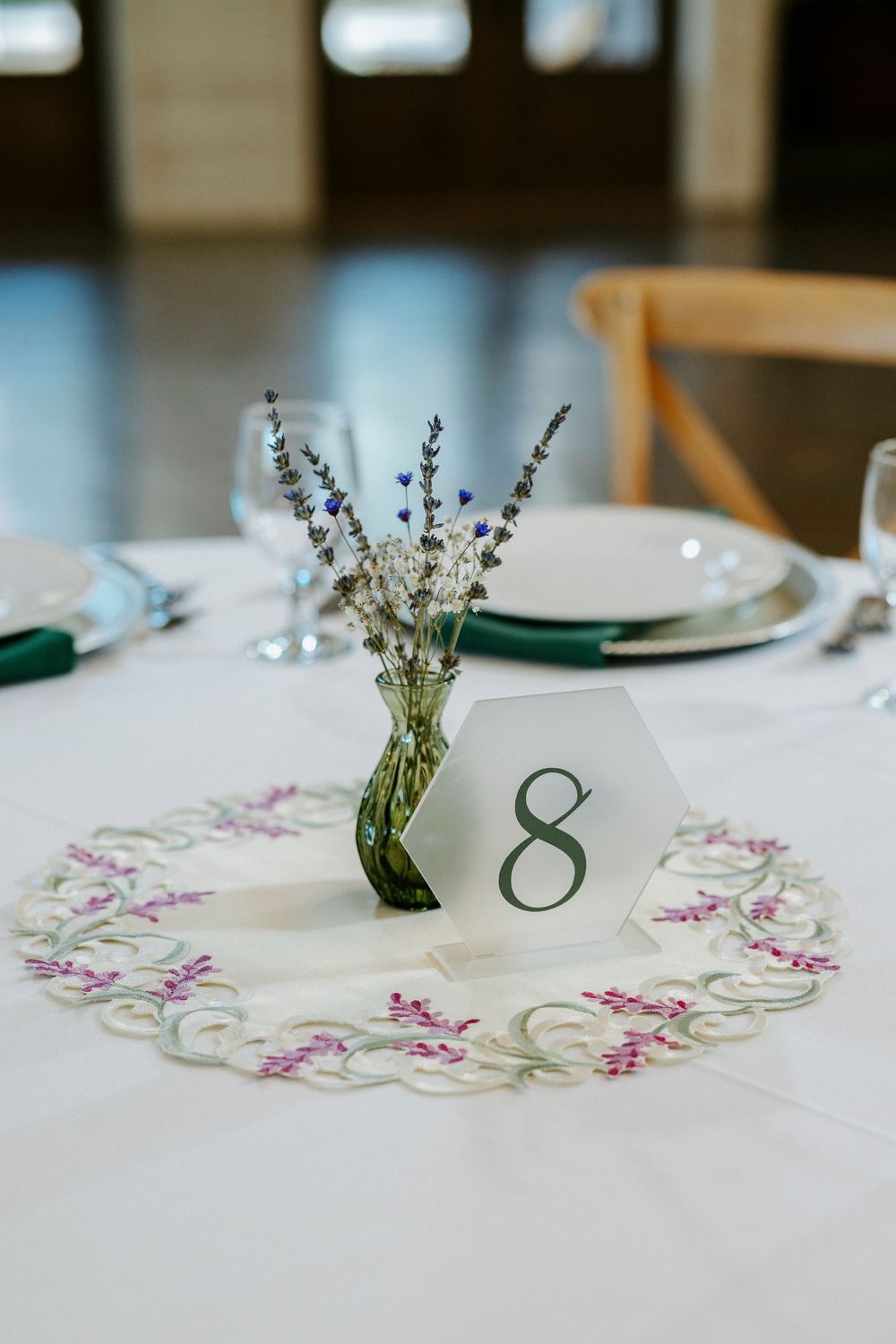 White table linens decorated with delicate floral embroidery and lavender sprigs in small white vases create an elegant place setting.