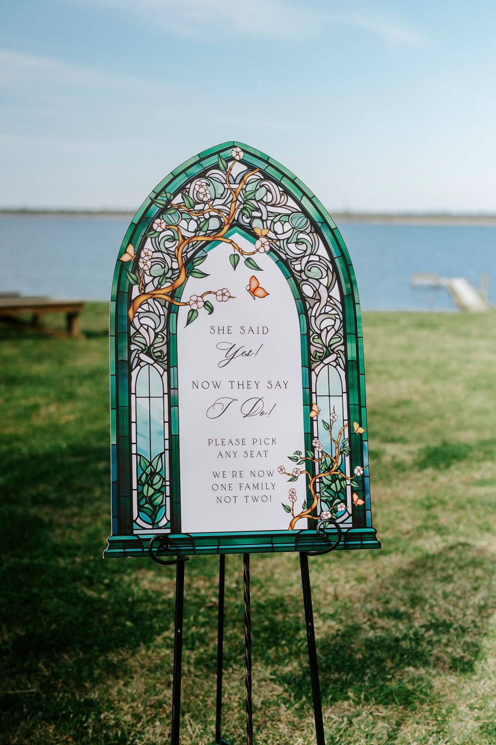 Decorative garden arch signs with floral designs and text displayed on grass against a blue sky background.