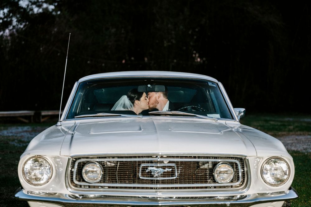 Classic white Ford Mustang convertible parked outdoors during a wedding celebration.