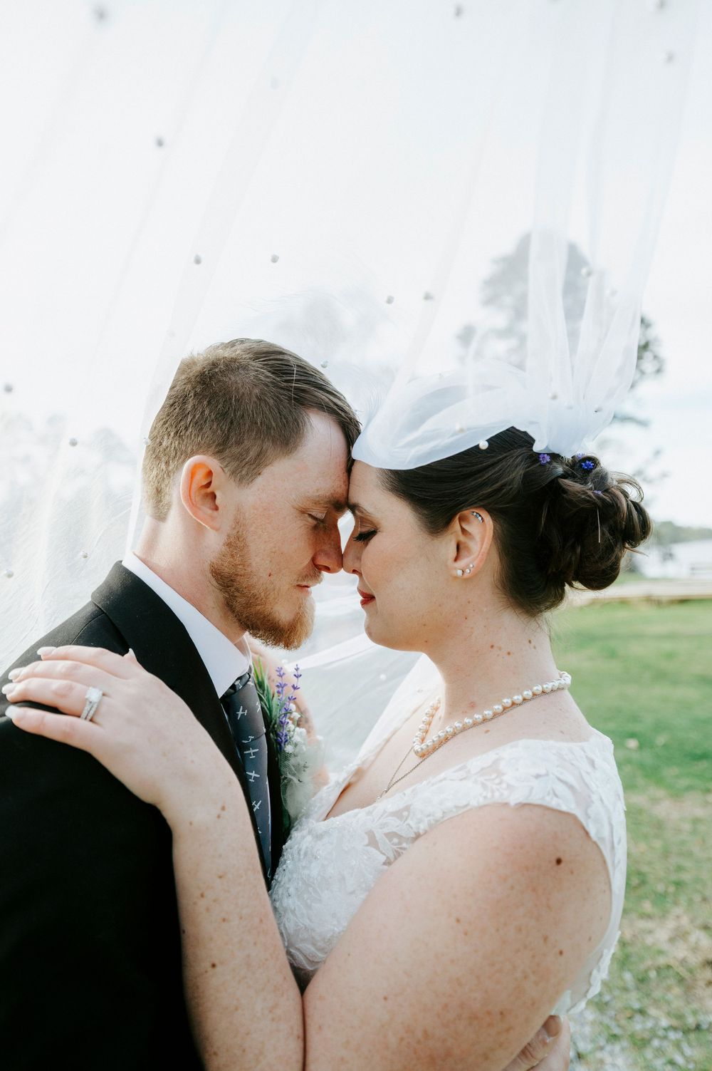Intimate wedding portrait showing tender forehead touching moment between newlyweds in romantic outdoor setting.