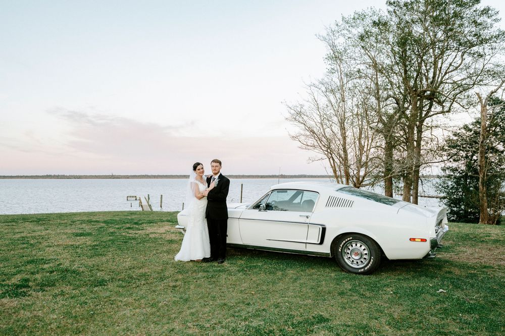 A classic white limousine parked in a grassy field at sunset with figures standing beside it.