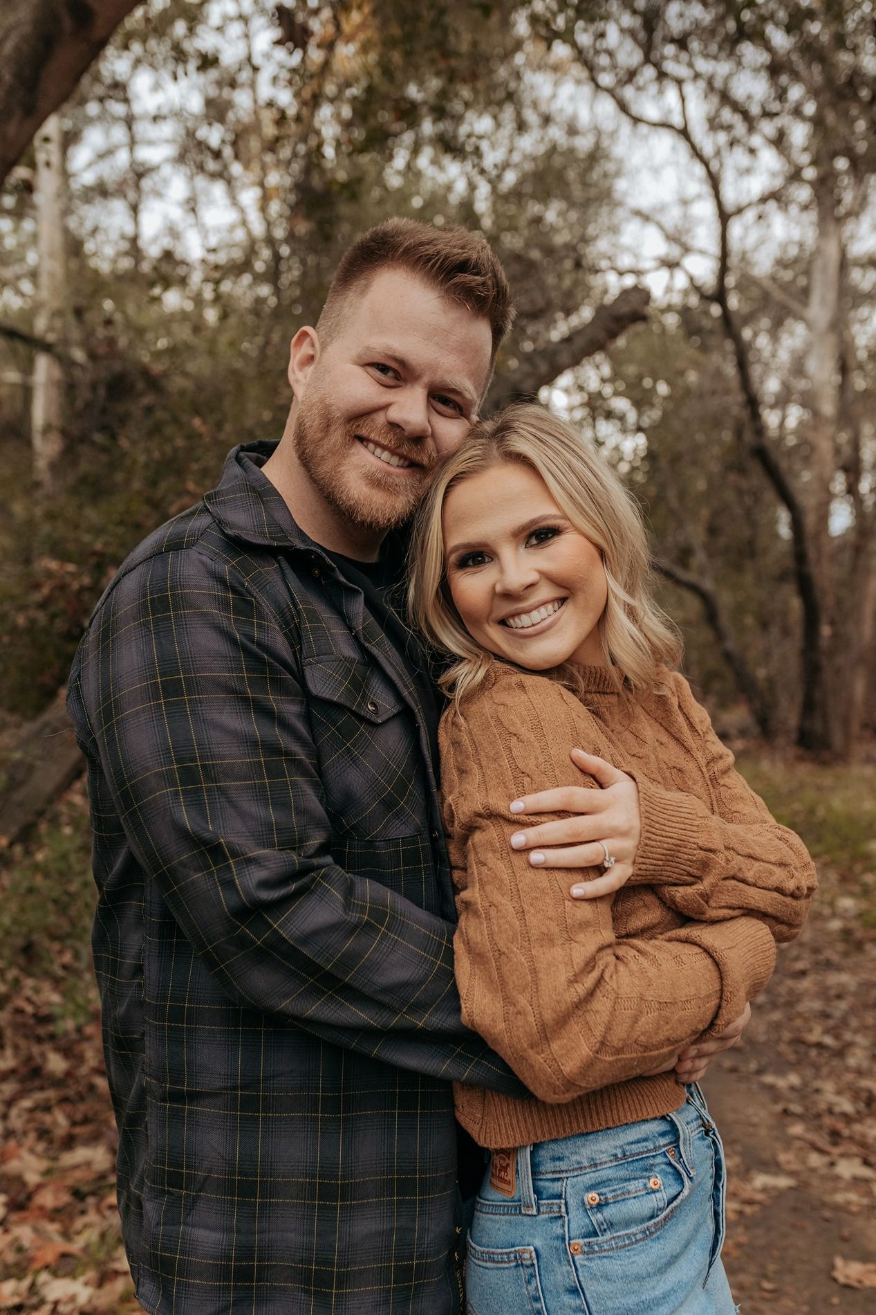 Couple embraces in autumn woods wearing casual attire of flannel and denim during outdoor photoshoot in San Diego.