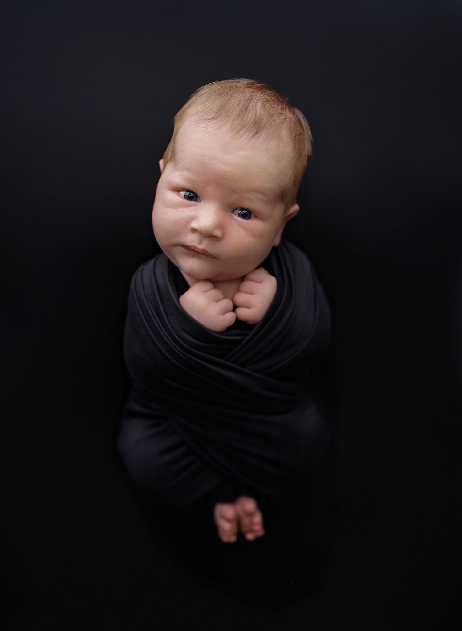 A photo of a newborn baby boy wrapped in a black swaddle