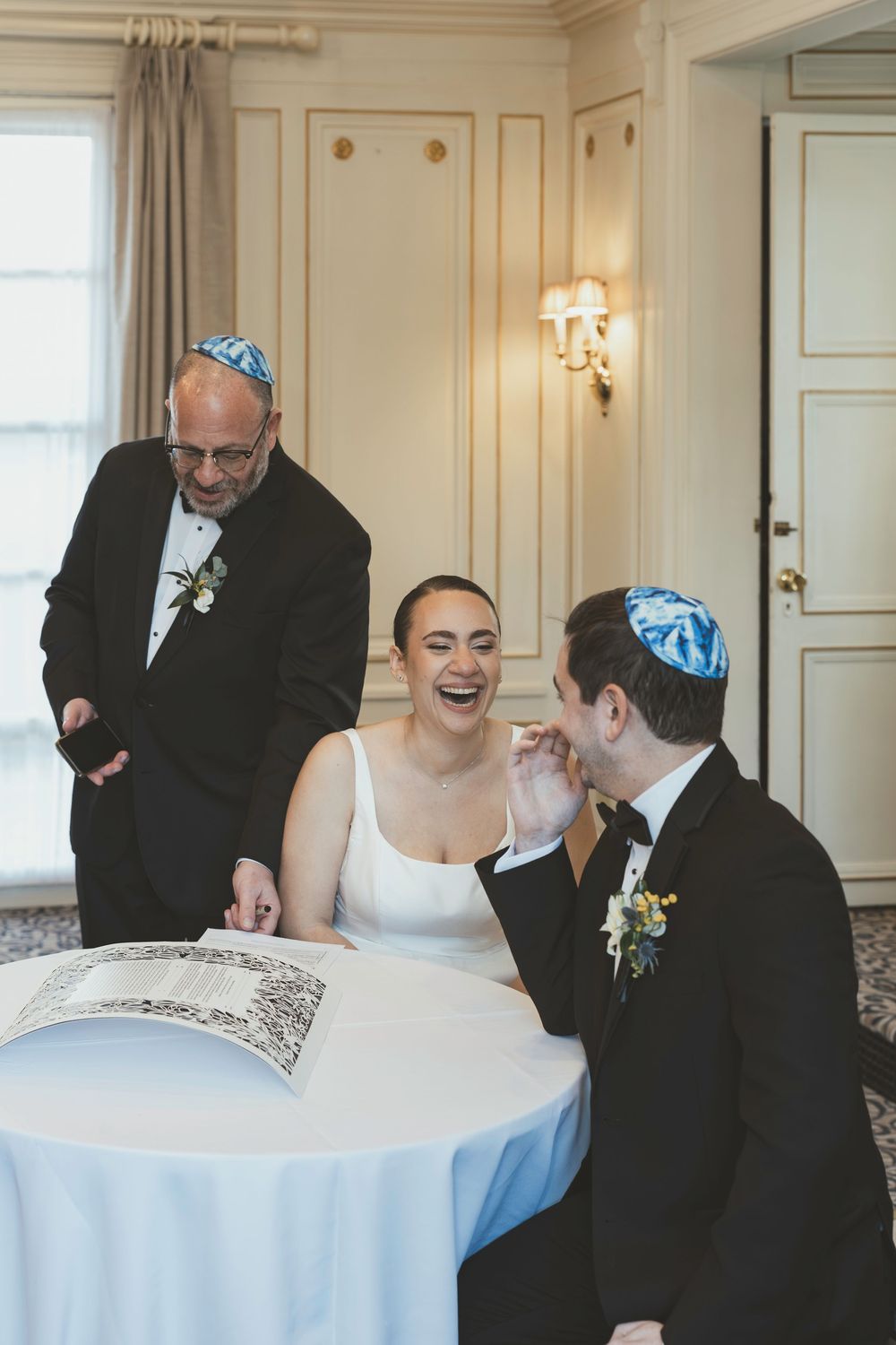 A joyous moment at a wedding reception showing laughter and celebration around a white-clothed table.