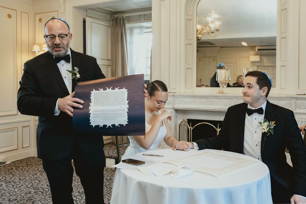 Wedding ceremony guests signing a document at an elegant venue with ornate decor and white tablecloths.