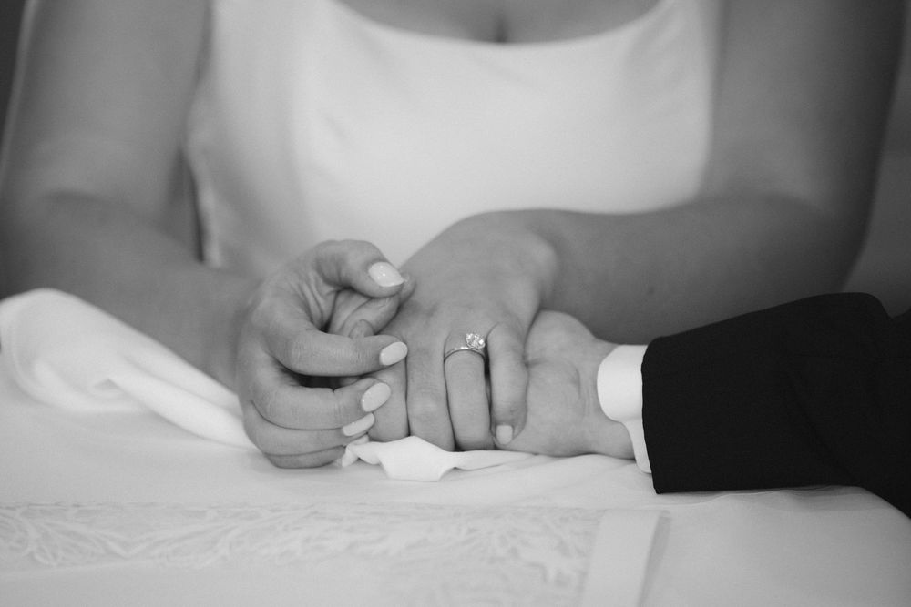 Black and white close-up of hands exchanging wedding rings during a marriage ceremony.