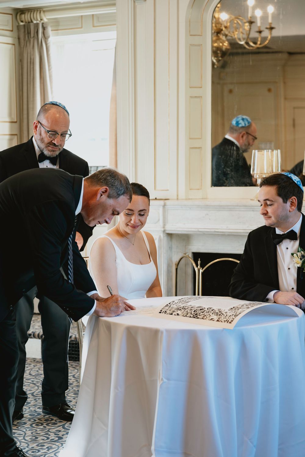 A couple signs their wedding ketubah during a traditional Jewish ceremony at an elegant venue.