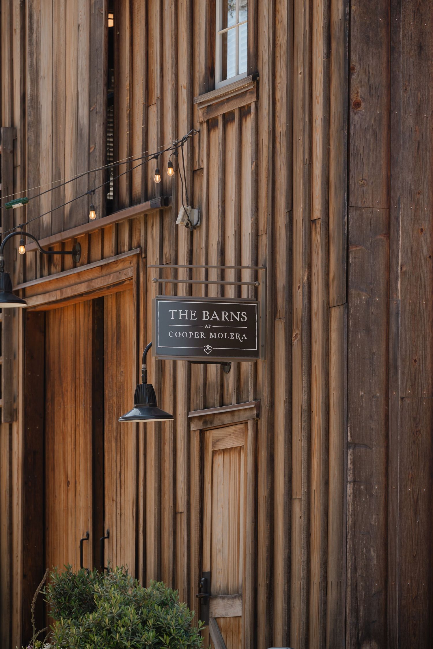 Rustic wooden barn exterior with vertical planks and 'The Barns' signage mounted on wall.