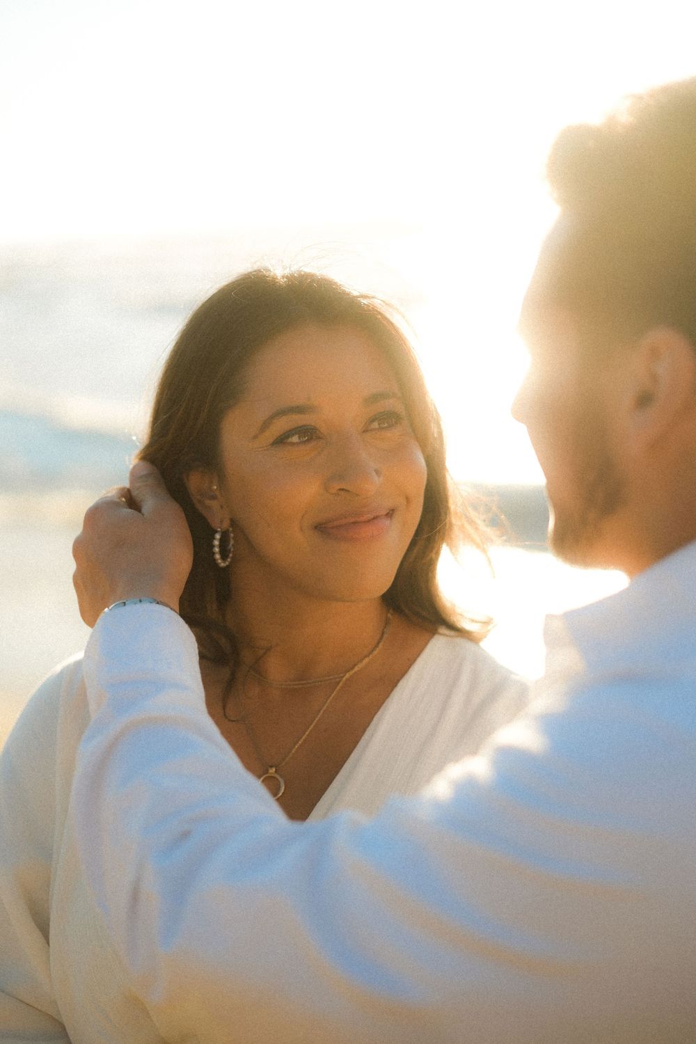 Sun-kissed portrait of a couple in white clothing at the beach.