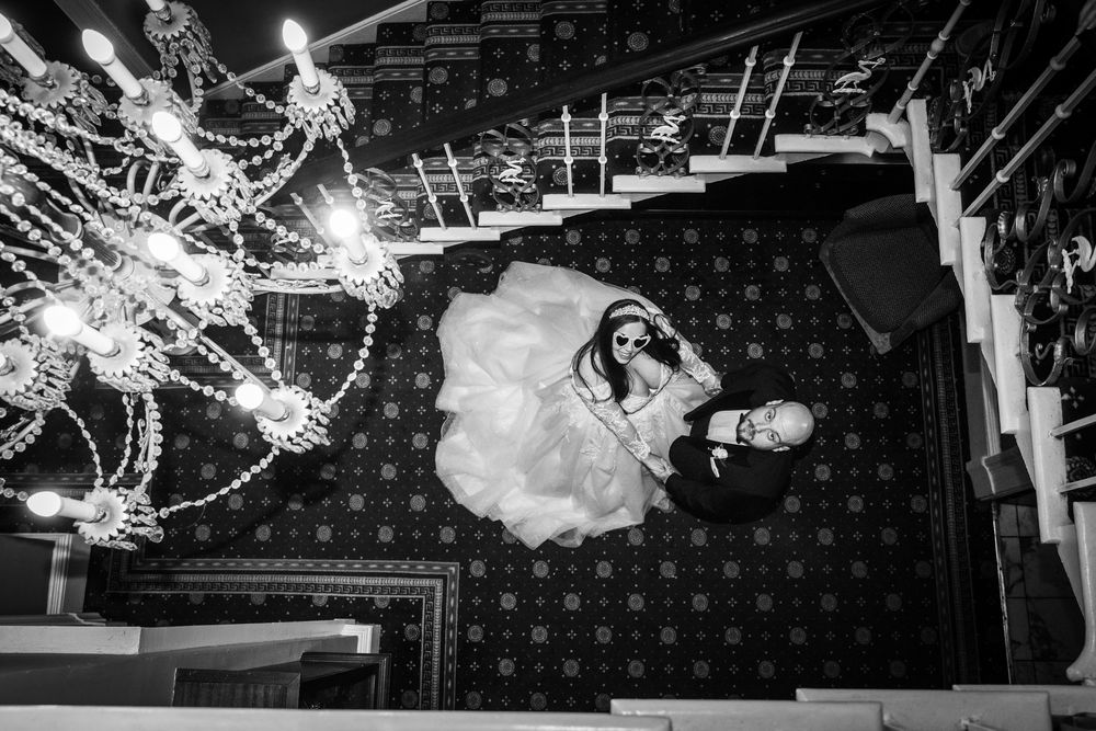 Stunning black and white aerial shot of bride and groom lying on ornate floor beneath crystal chandelier.