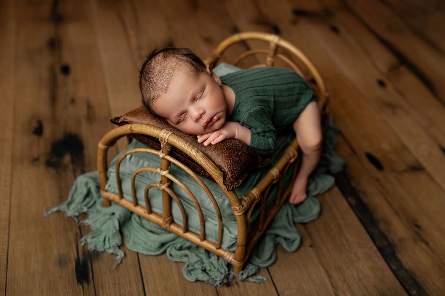 Newborn baby boy in green romper posing on bamboo rainbow bed at Flowertown Photography Studio in Summerville, SC