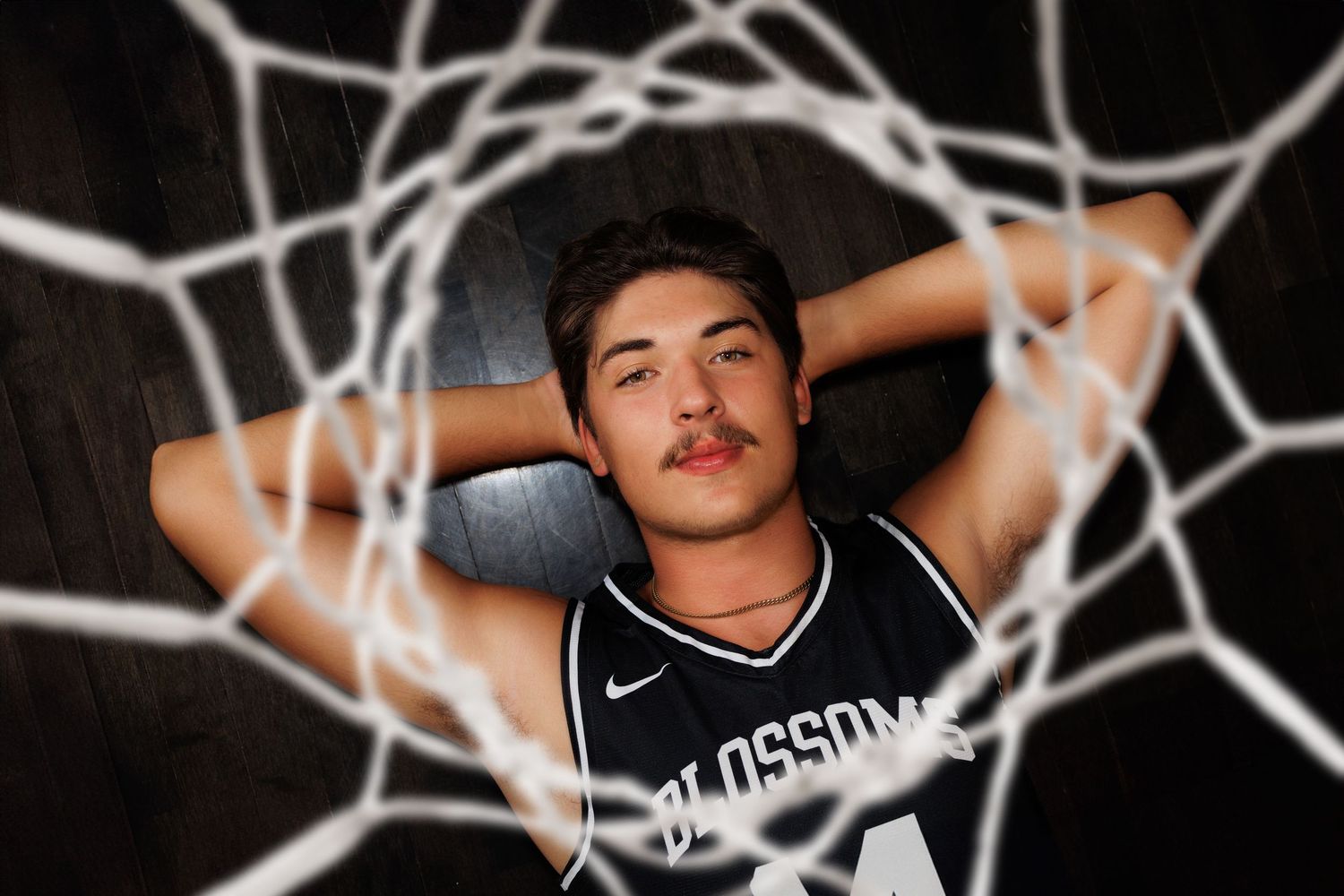 Senior basketball player in black jersey poses with a basketball hoop net