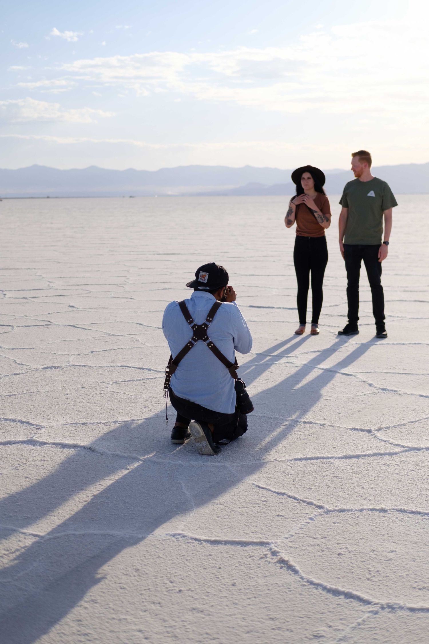 Photographer crouching to capture people casting long shadows on the white hexagonal patterns of Bonneville Salt Flats.