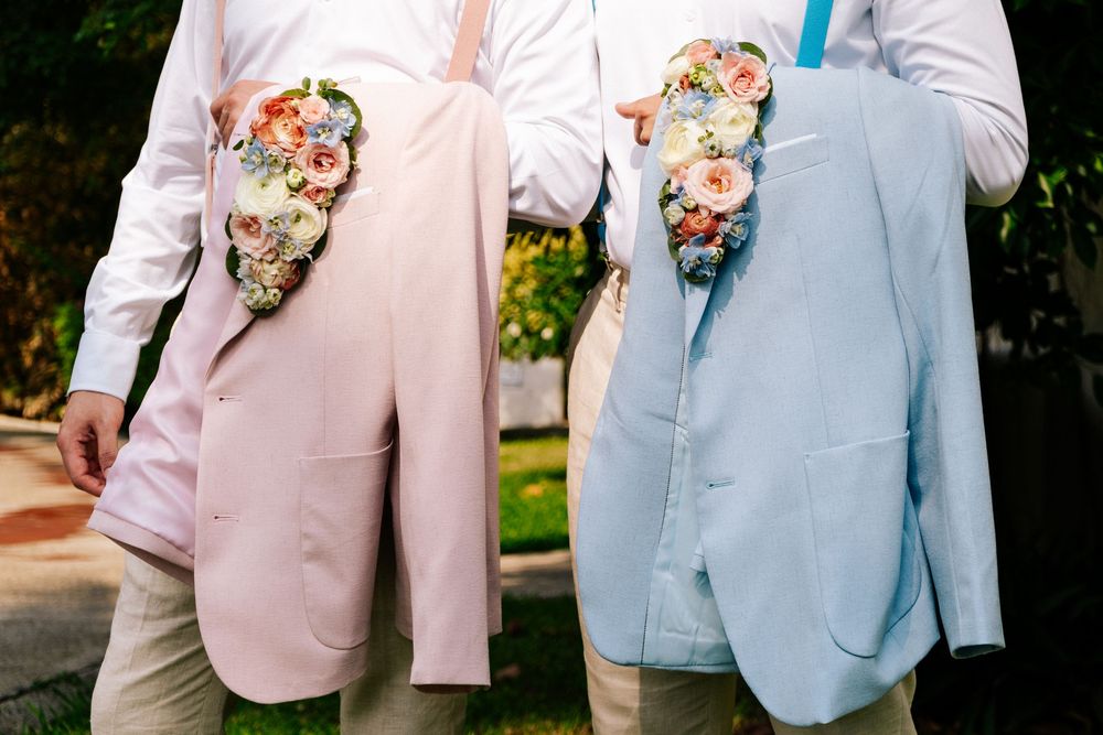 Two people wearing pastel pink and blue suits with floral boutonnieres standing side by side outdoors.