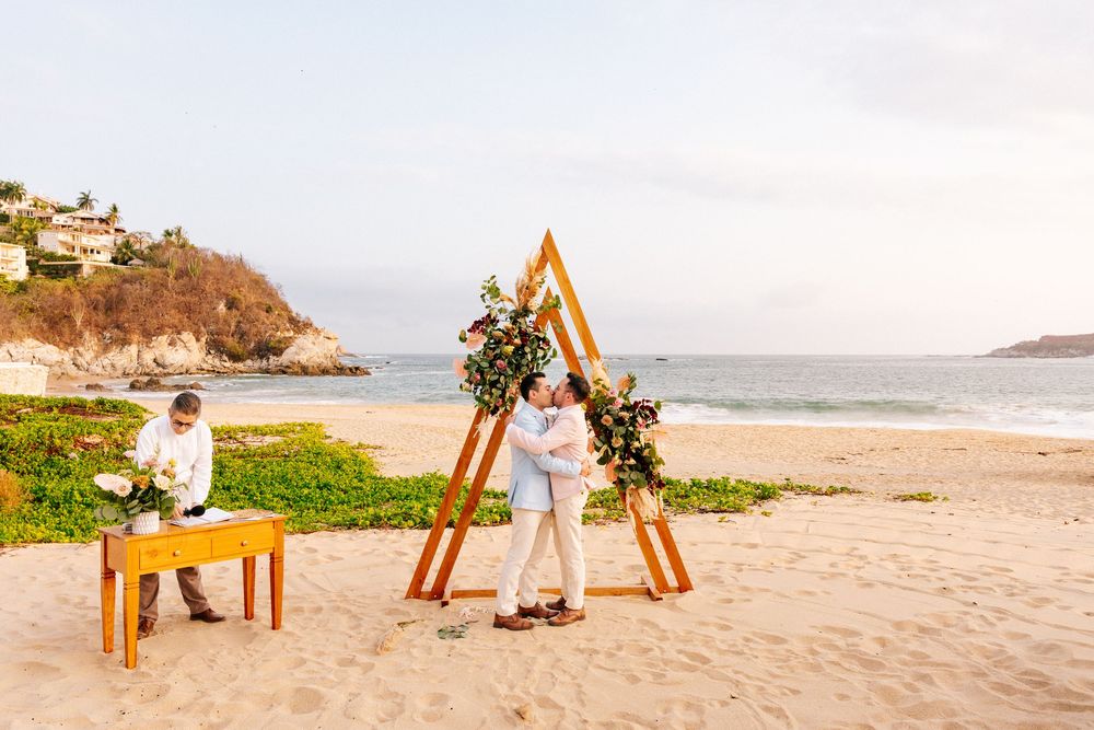 Artist painting on easel at scenic tropical beach during golden hour with ocean and cliffs in background.
