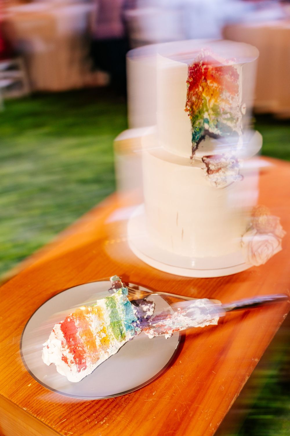 Rainbow-colored wedding cake slices displayed on white plates atop a wooden surface.