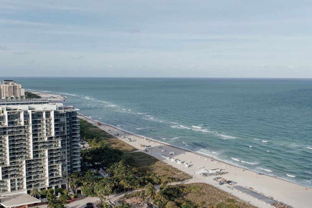 Serene aerial view of sandy beach meeting calm turquoise ocean under partly cloudy sky.