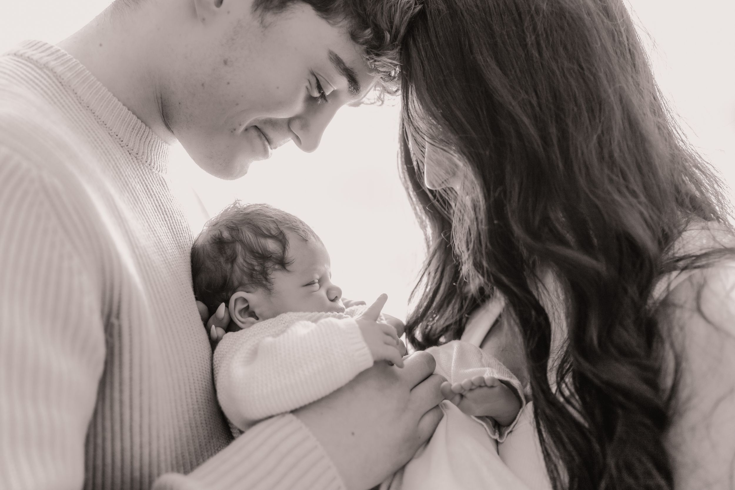 A tender black and white portrait of parents with their newborn baby in an intimate family moment.