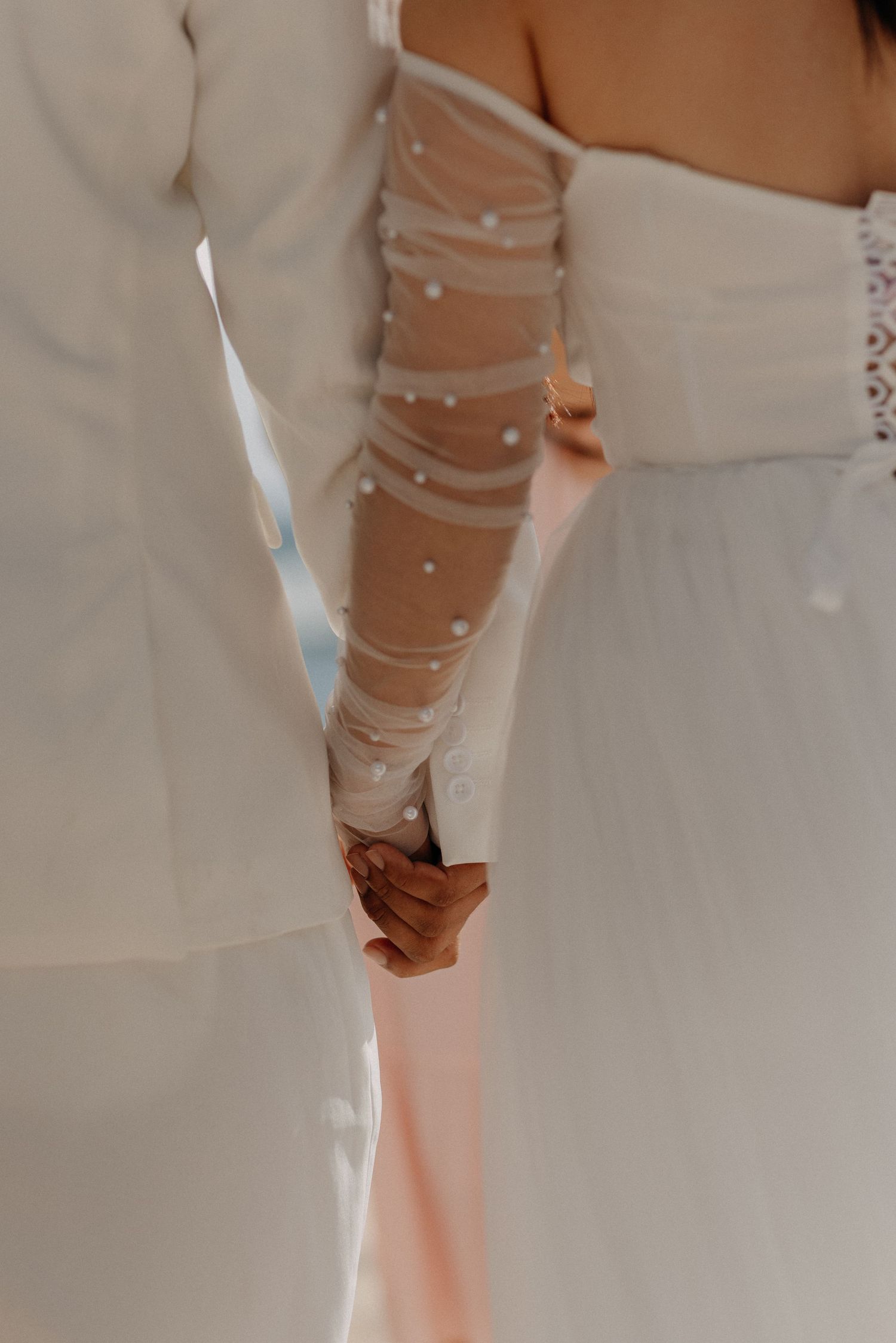 A couple in white attire shares a romantic moment on a scenic beach with crashing waves in the background.