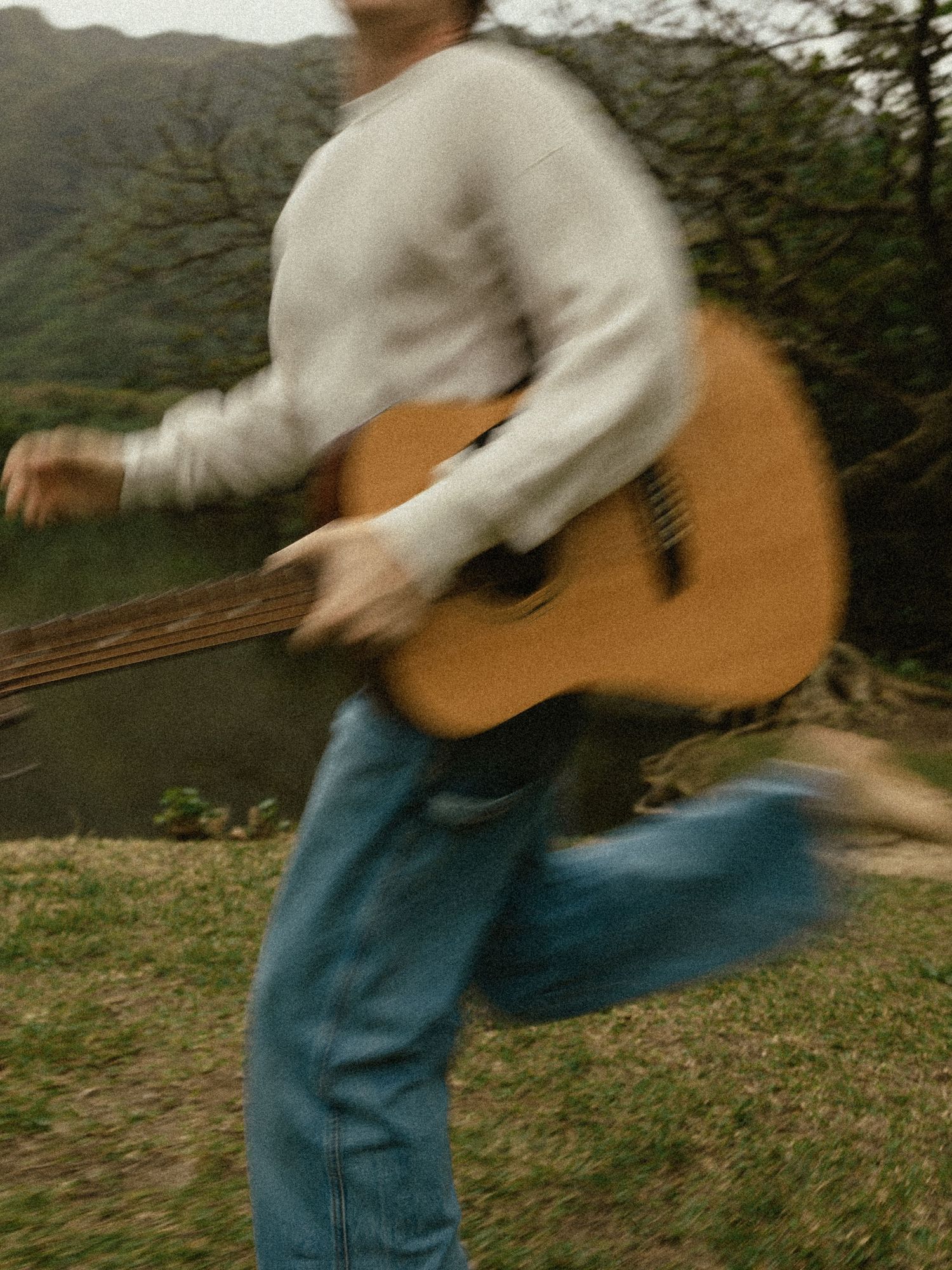 A sequence of motion blur photos showing someone in blue jeans swinging an acoustic guitar in an outdoor setting.
