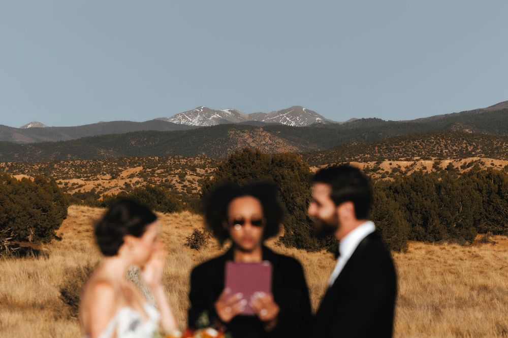Bride and groom in soft focus with officiant and snow-capped mountains in background during ceremony.